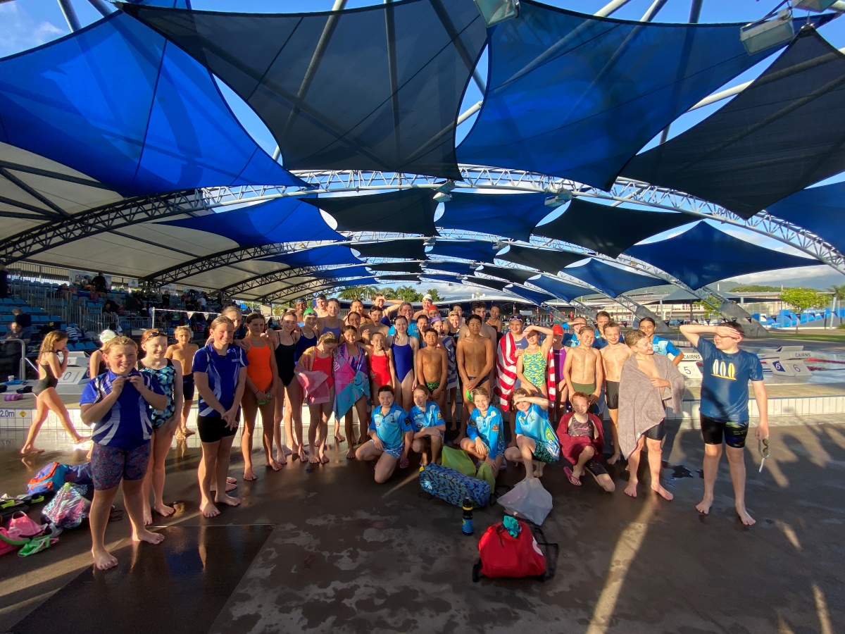 A group of swimmers in swimwear and gathered at a swimming pool for a clinic