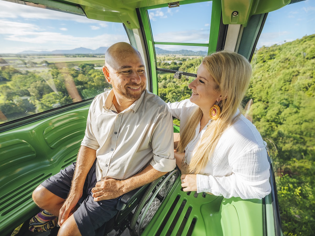 A couple sitting in a skyrail cabin, suspended high above a lush forest canopy