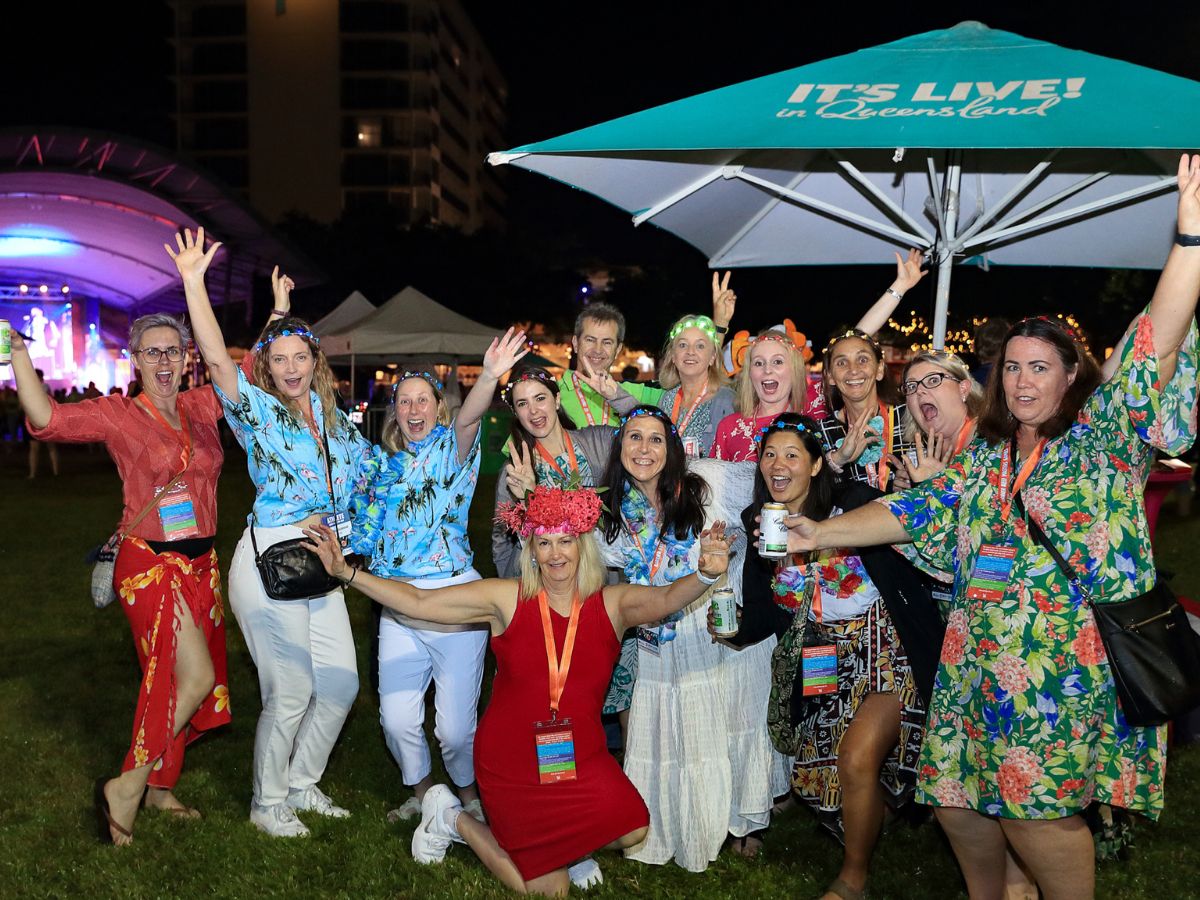 A group of masters competitors smiling and posing for a photo at an event, with vibrant, colorful lighting and decorations in the background