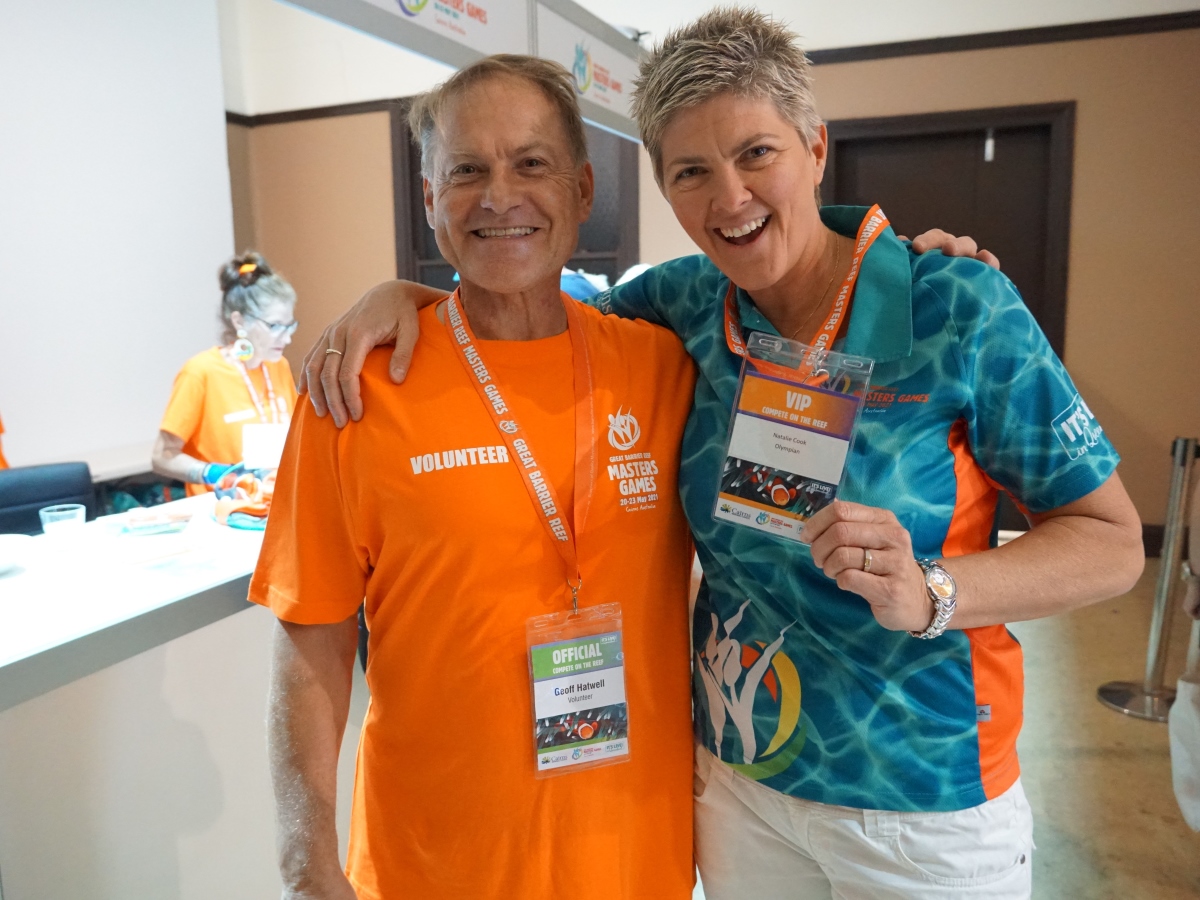 A volunteer standing beside a games ambassador, both smiling at the camera